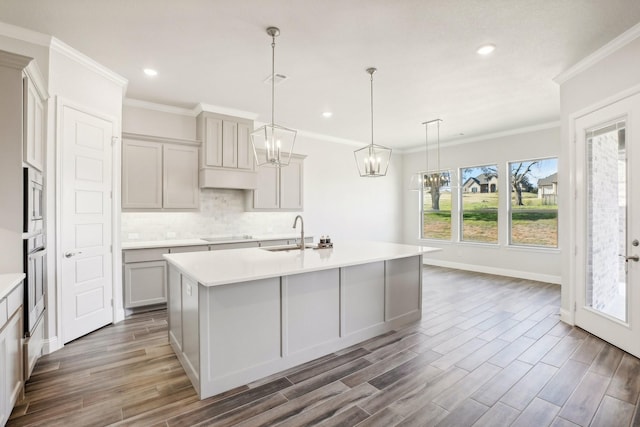 kitchen with hanging light fixtures, sink, an island with sink, and gray cabinetry