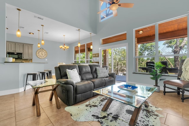 living room with a high ceiling, light tile flooring, and ceiling fan with notable chandelier