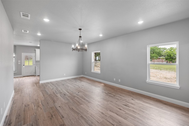 empty room with a notable chandelier, light wood-type flooring, and a textured ceiling