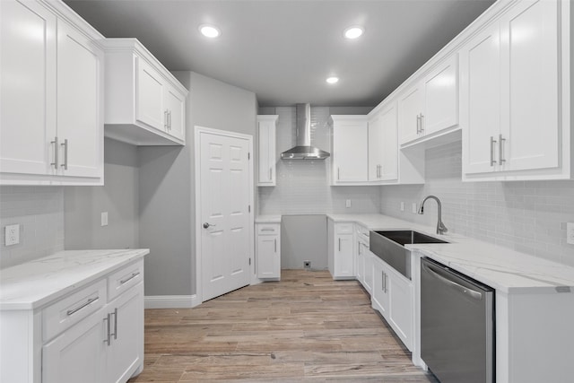 kitchen with white cabinets, wall chimney range hood, sink, stainless steel dishwasher, and light wood-type flooring