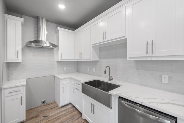 kitchen with light wood-type flooring, stainless steel dishwasher, sink, wall chimney range hood, and white cabinets