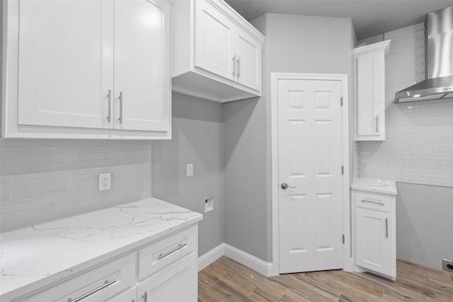 kitchen with white cabinets, decorative backsplash, light stone countertops, and wall chimney range hood