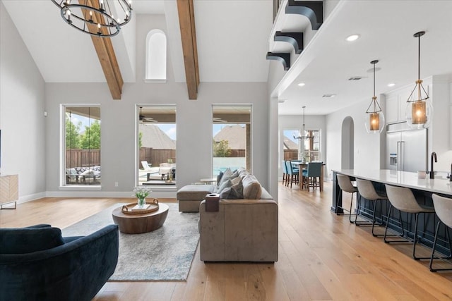 living room with sink, a chandelier, high vaulted ceiling, light wood-type flooring, and beam ceiling