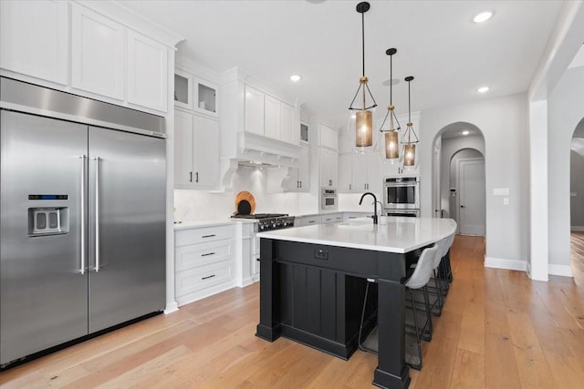 kitchen featuring sink, premium range hood, appliances with stainless steel finishes, an island with sink, and white cabinets