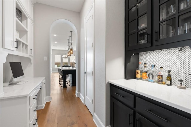 bar with backsplash, white cabinets, light stone counters, and light hardwood / wood-style floors