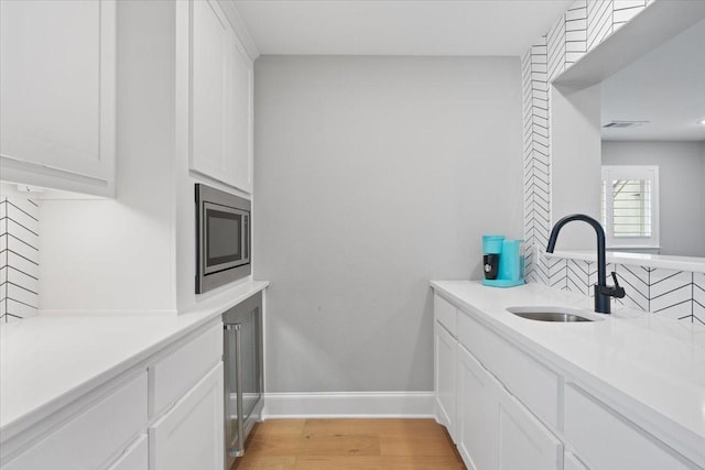 kitchen with sink, white cabinetry, stainless steel microwave, tasteful backsplash, and light wood-type flooring