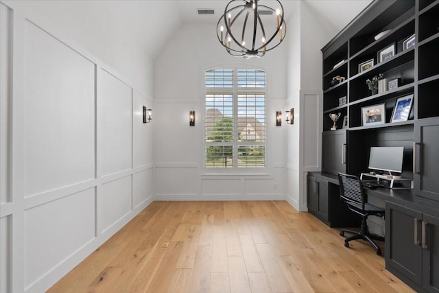 office space featuring lofted ceiling, a notable chandelier, built in shelves, and light wood-type flooring