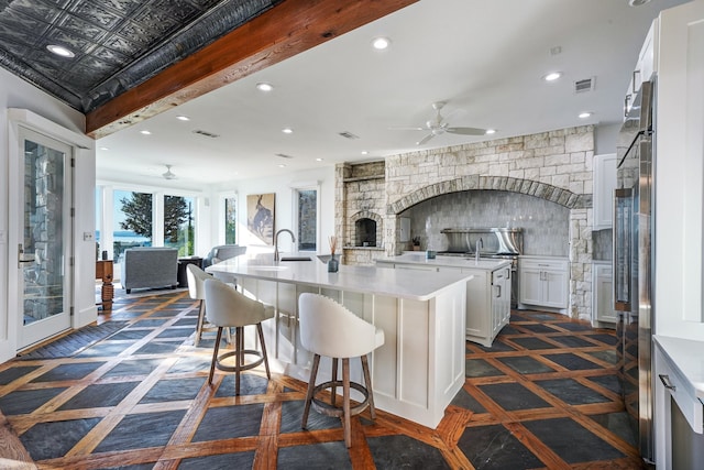 kitchen with a breakfast bar, white cabinets, ceiling fan, a fireplace, and a center island with sink