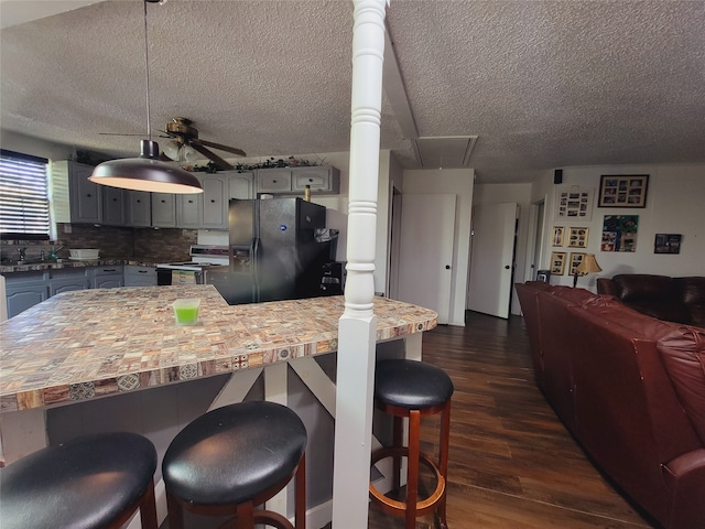 kitchen featuring a textured ceiling, dark wood-type flooring, black refrigerator with ice dispenser, backsplash, and gas range gas stove