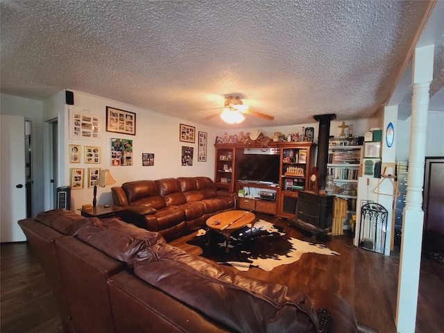 living room featuring a textured ceiling, wood-type flooring, ceiling fan, and a wood stove