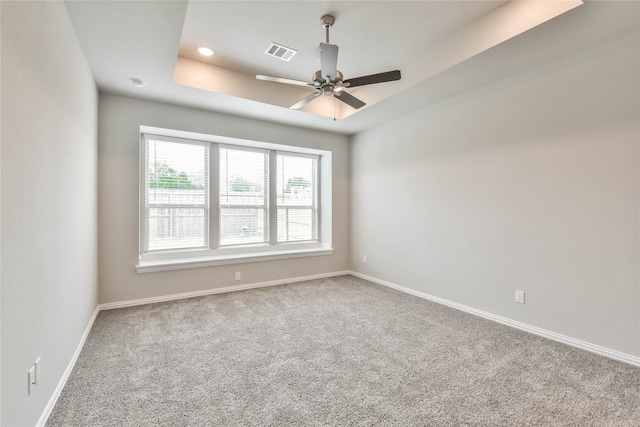 carpeted empty room with a raised ceiling and ceiling fan