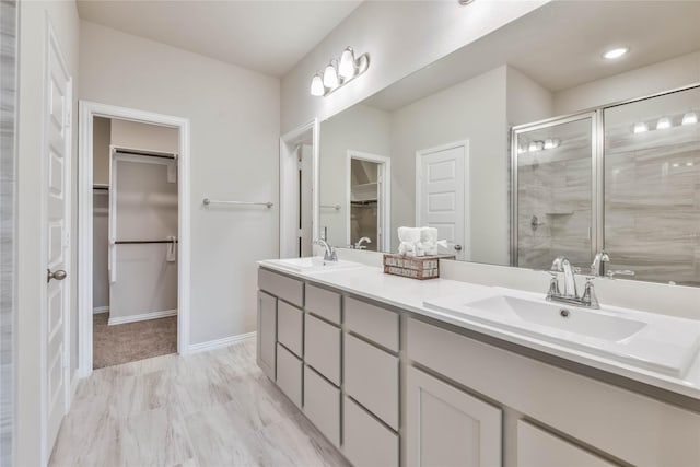full bathroom featuring a stall shower, double vanity, a sink, and a walk in closet