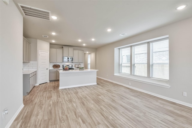 kitchen with light wood-style flooring, gray cabinetry, visible vents, decorative backsplash, and appliances with stainless steel finishes