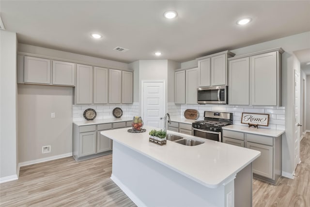 kitchen featuring baseboards, an island with sink, gray cabinetry, and stainless steel appliances
