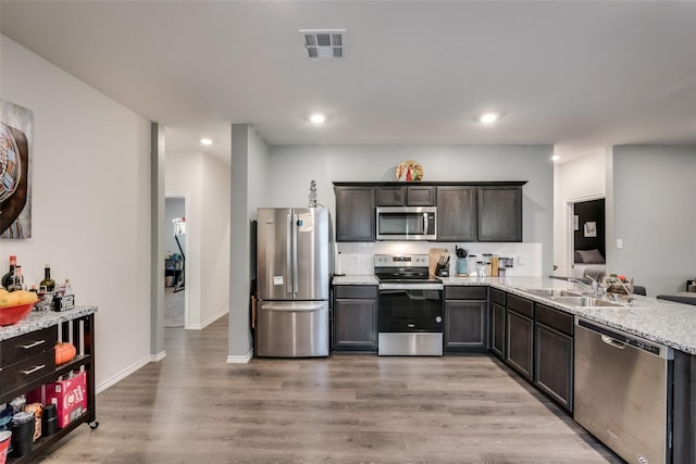 kitchen with light hardwood / wood-style floors, light stone countertops, stainless steel appliances, dark brown cabinets, and sink