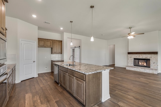 kitchen featuring light stone counters, a kitchen island with sink, dark hardwood / wood-style floors, sink, and a barn door