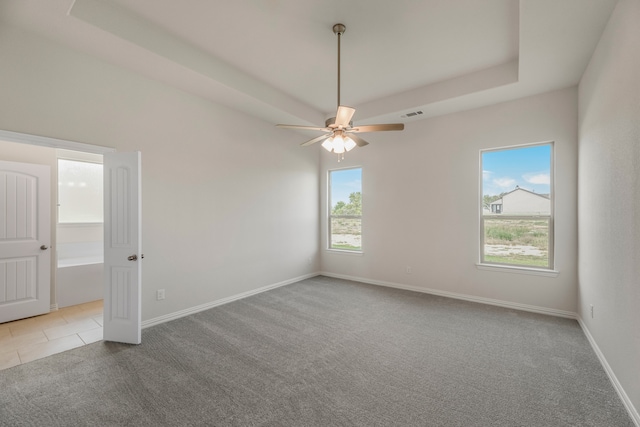 carpeted empty room with a raised ceiling and ceiling fan