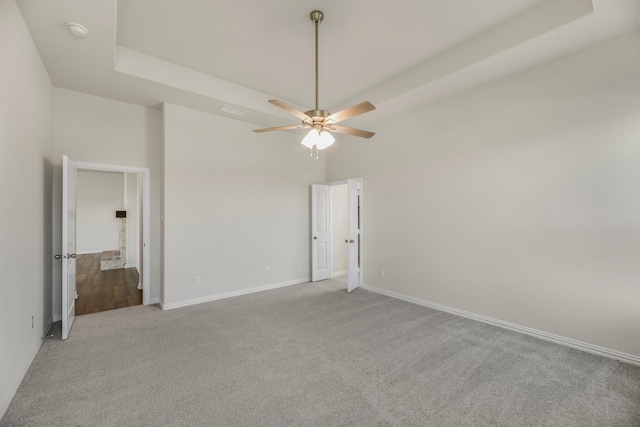 carpeted empty room featuring ceiling fan and a raised ceiling