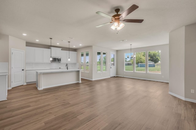 unfurnished living room featuring ceiling fan with notable chandelier, light wood finished floors, recessed lighting, and baseboards