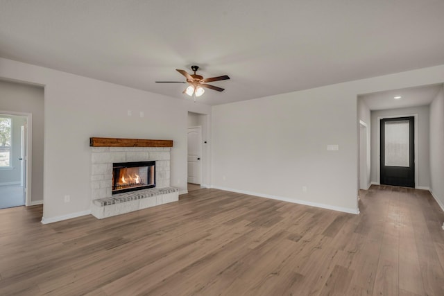 unfurnished living room with a ceiling fan, baseboards, wood finished floors, and a stone fireplace