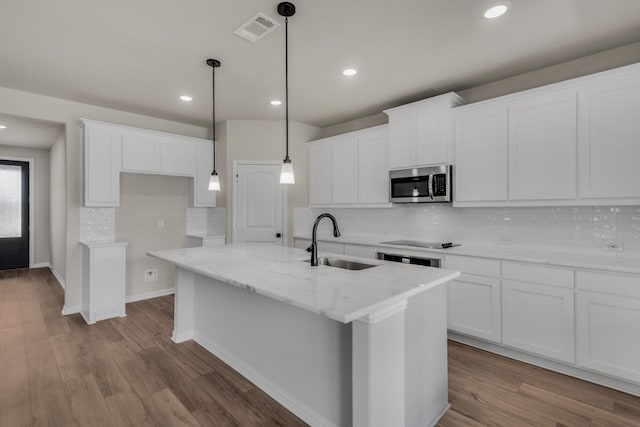 kitchen featuring a center island with sink, stainless steel microwave, visible vents, a sink, and wood finished floors