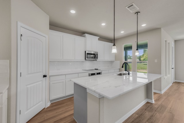 kitchen featuring decorative backsplash, white cabinets, an island with sink, sink, and light hardwood / wood-style flooring