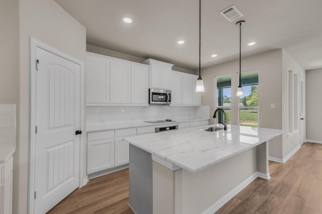 kitchen with a sink, visible vents, light wood-style floors, stainless steel microwave, and an island with sink