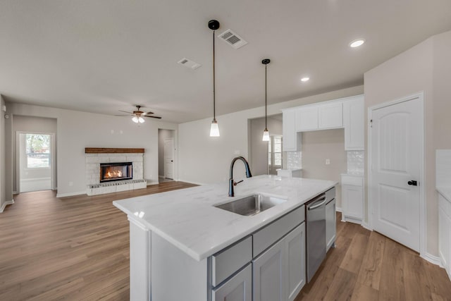 kitchen with light wood finished floors, visible vents, stainless steel dishwasher, a sink, and a stone fireplace