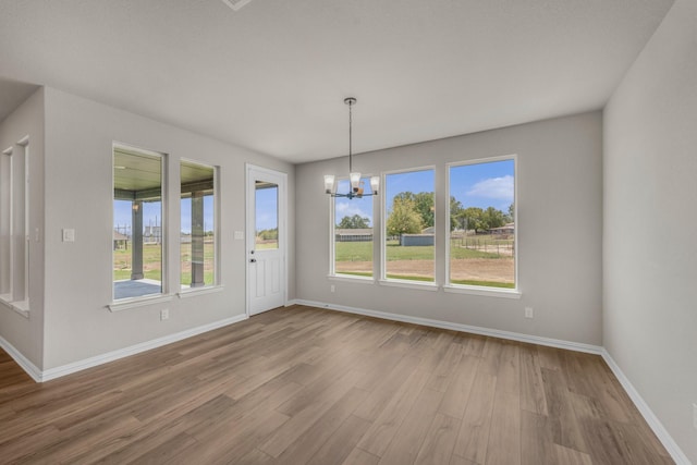 unfurnished dining area with a chandelier, baseboards, and wood finished floors