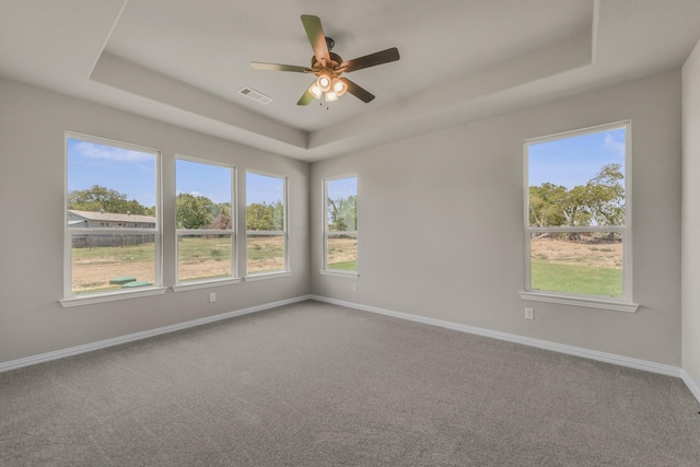 empty room with visible vents, a tray ceiling, baseboards, and carpet flooring