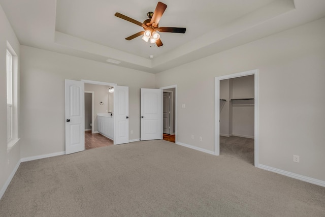 unfurnished bedroom with a walk in closet, baseboards, a raised ceiling, and carpet flooring