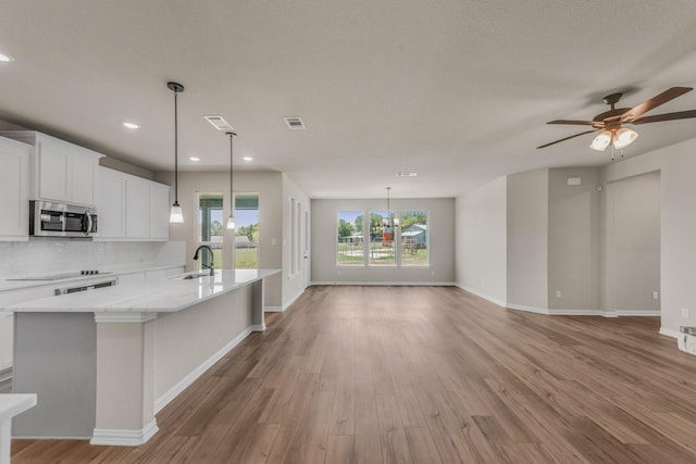 kitchen with light wood finished floors, tasteful backsplash, an island with sink, stainless steel microwave, and a sink