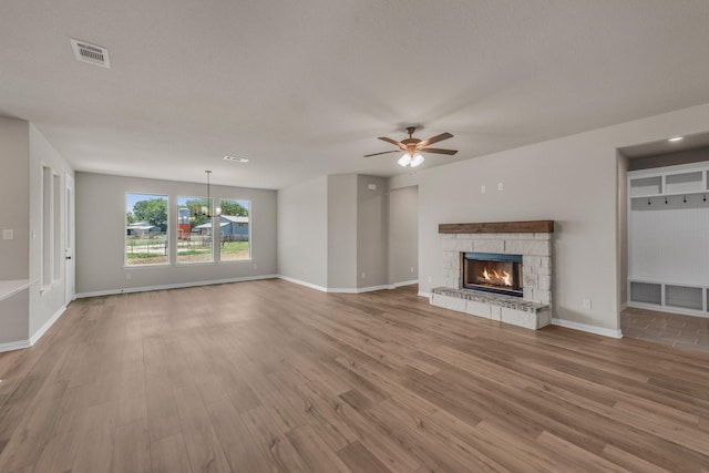 unfurnished living room with a fireplace, visible vents, light wood-style floors, baseboards, and ceiling fan with notable chandelier