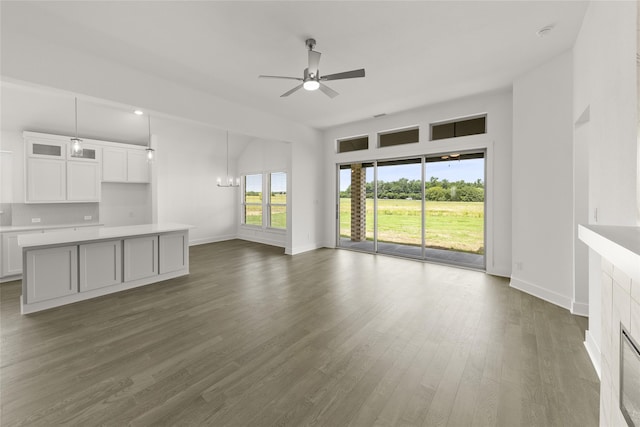 unfurnished living room with ceiling fan with notable chandelier, a fireplace, and dark hardwood / wood-style floors