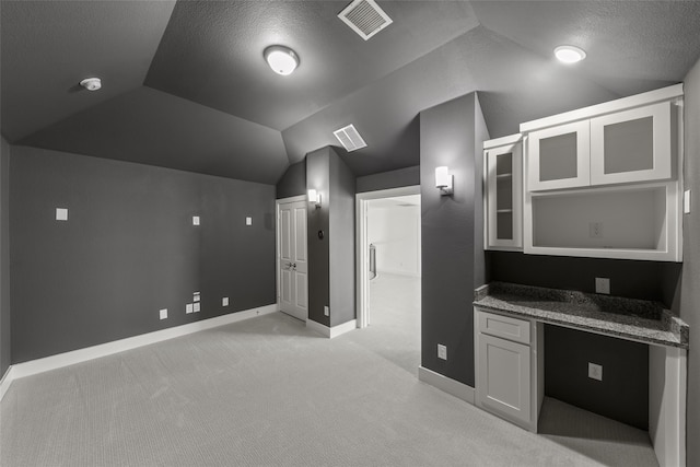 kitchen featuring lofted ceiling, stone counters, built in desk, a textured ceiling, and light carpet