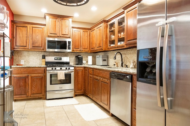 kitchen featuring stainless steel appliances, light stone countertops, sink, and decorative backsplash