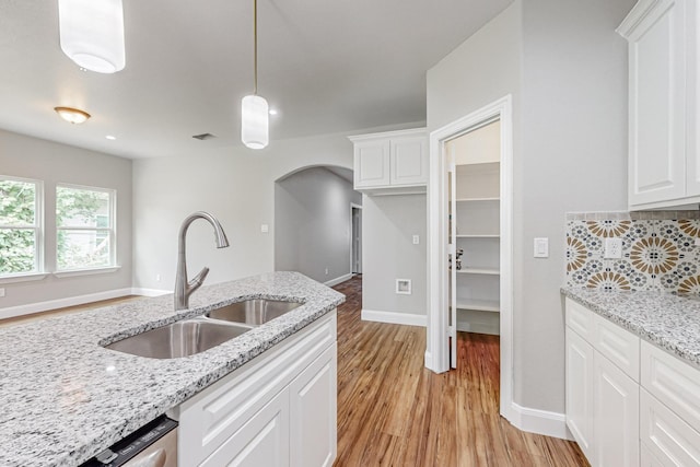 kitchen featuring light hardwood / wood-style flooring, sink, pendant lighting, white cabinets, and light stone countertops