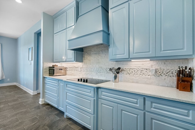 kitchen featuring custom range hood, blue cabinetry, black electric stovetop, and backsplash