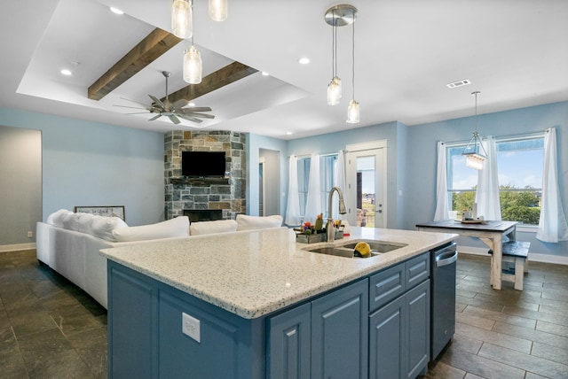 kitchen featuring beamed ceiling, sink, a stone fireplace, and an island with sink