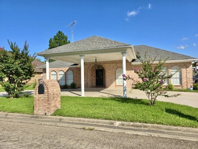 back of property with a shingled roof, brick siding, and a lawn