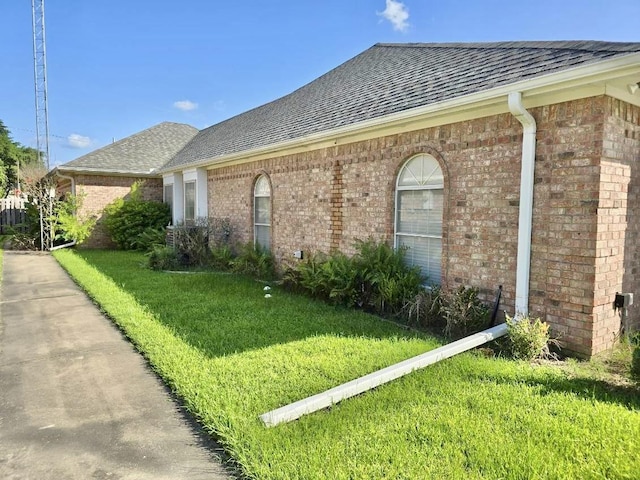 single story home with a shingled roof, a front lawn, and brick siding