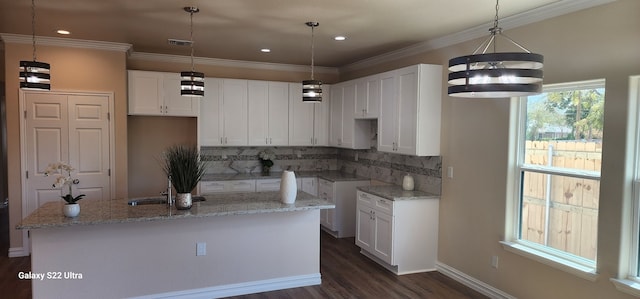 kitchen with white cabinetry, backsplash, light stone countertops, and a center island with sink