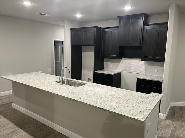 kitchen featuring sink, backsplash, wood-type flooring, and a kitchen island with sink