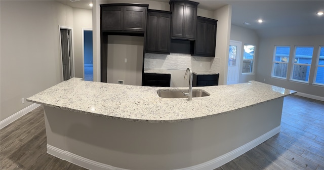 kitchen featuring light stone countertops, an island with sink, dark hardwood / wood-style floors, backsplash, and sink