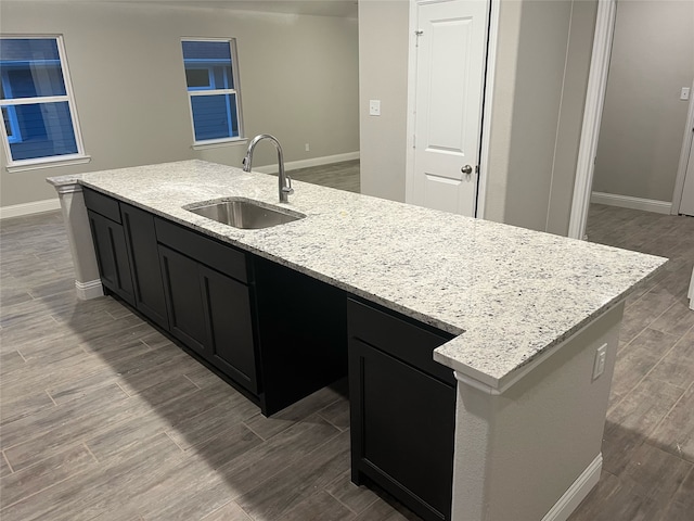 kitchen featuring sink, light stone countertops, and a center island with sink