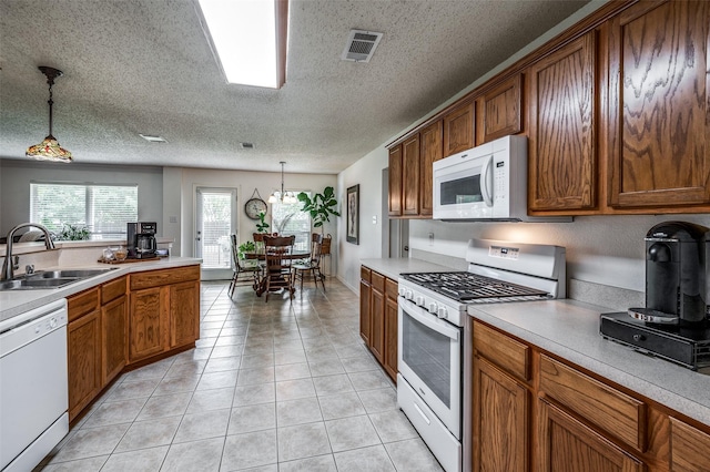 kitchen featuring decorative light fixtures, visible vents, light countertops, a sink, and white appliances