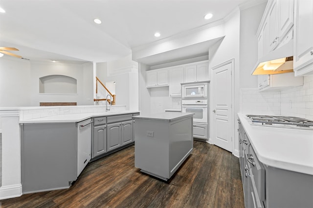 kitchen featuring white appliances, dark wood-type flooring, gray cabinets, a kitchen island, and backsplash