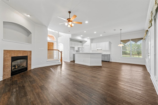 unfurnished living room featuring dark hardwood / wood-style flooring, a tiled fireplace, ceiling fan, and crown molding