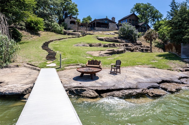 view of dock with a patio area, a water view, a fire pit, and a yard