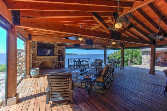 deck with ceiling fan, a water view, and an outdoor stone fireplace